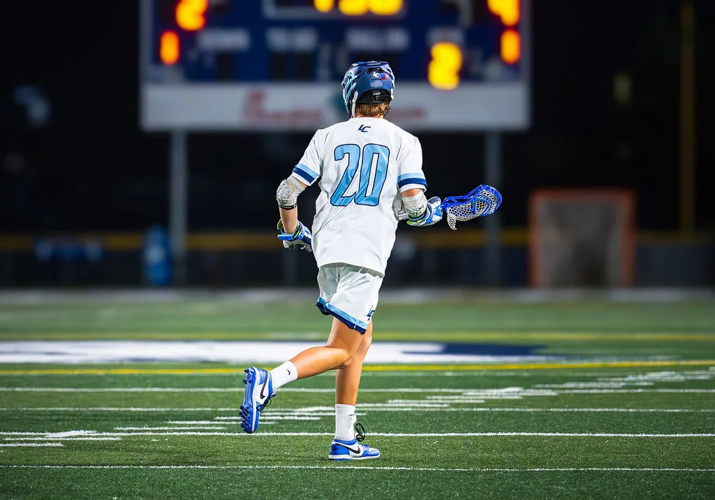 Lacrosse player under stadium lights with scoreboard in the background