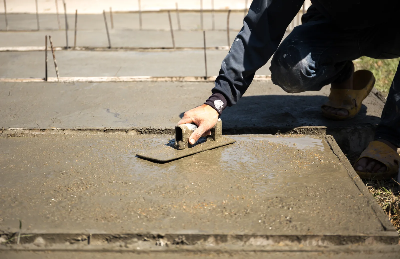 Concrete worker using a steel trowel to smooth and finish a concrete surface